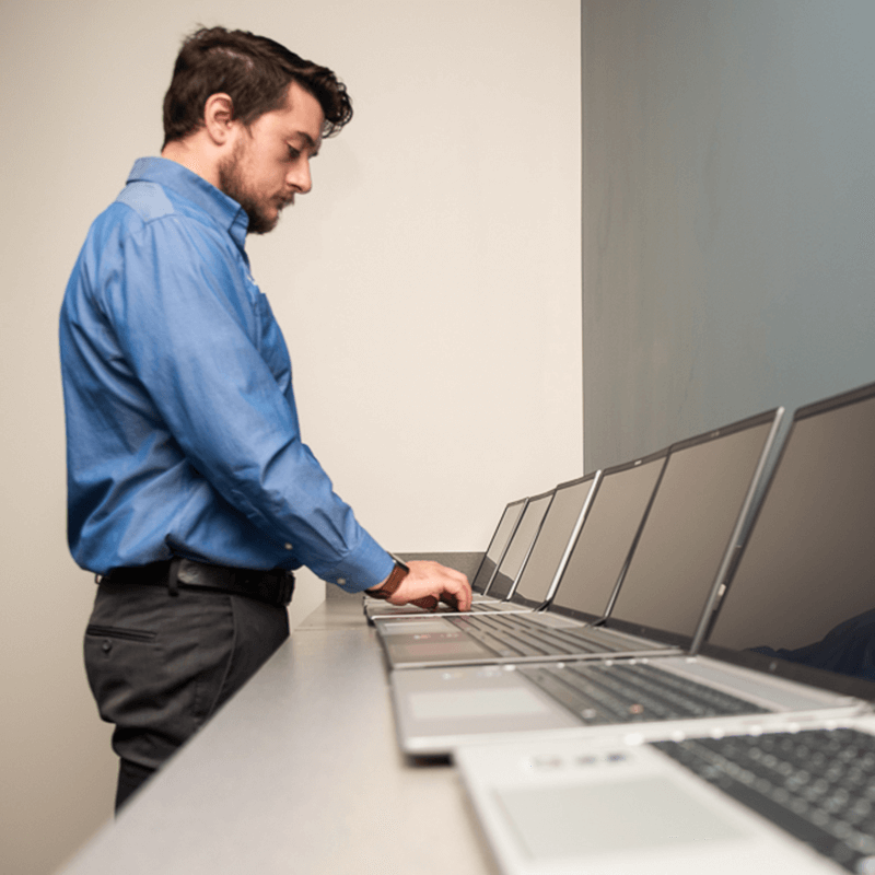 male IT employee standing over a line of laptops in perspective