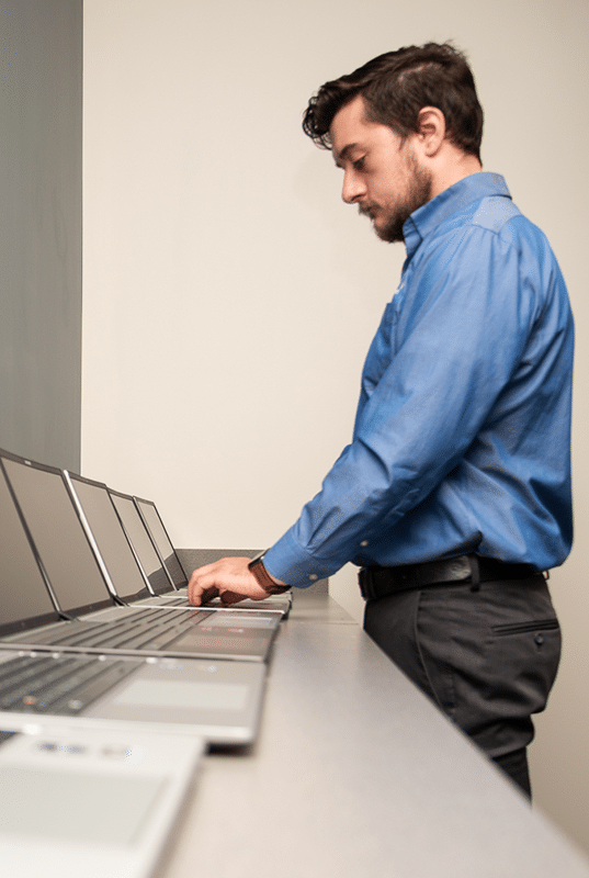 male IT worker typing on last laptop in row of laptops in perspective